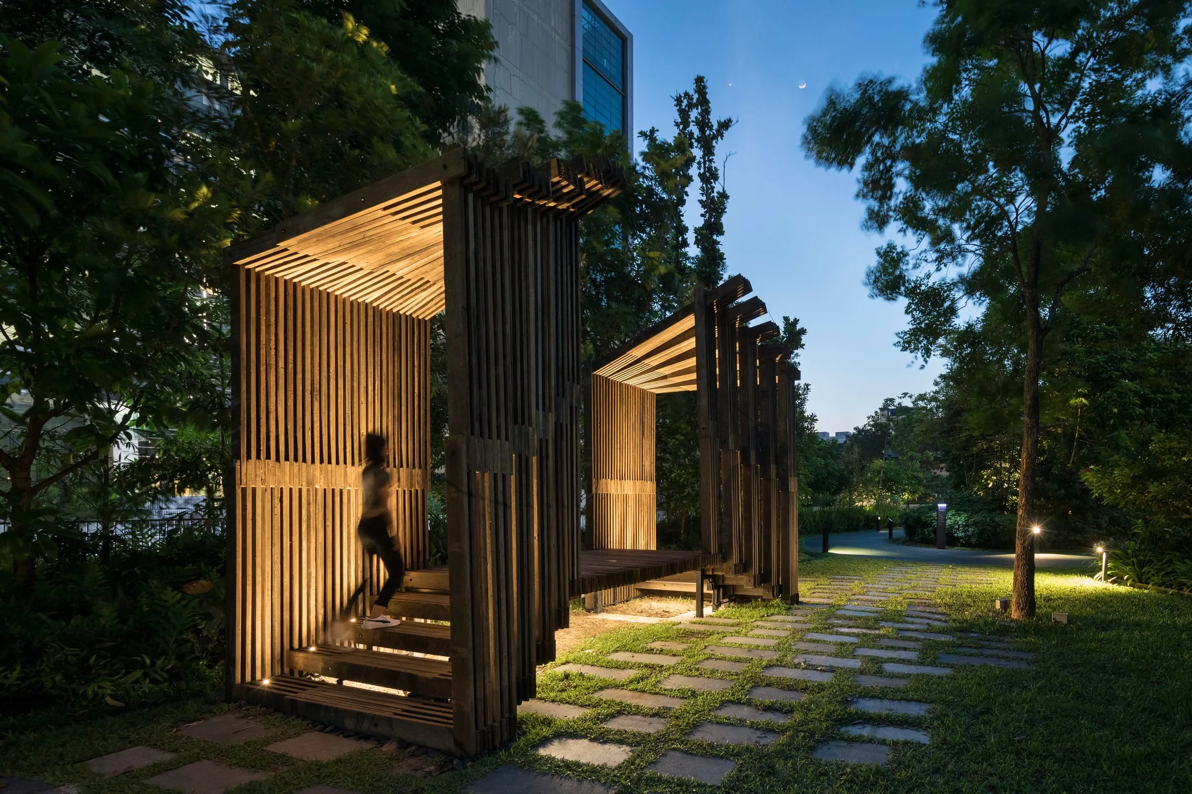 The Sundial Structure's slatted timber frames at dusk, with a figure climbing its steps